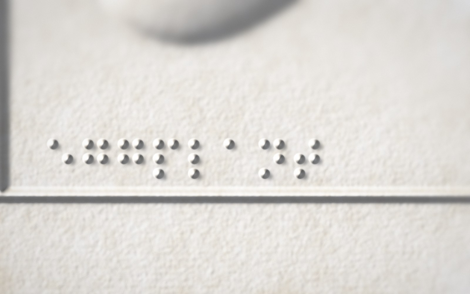 Close-up of a braille label beside a raised triangle marker on white cotton paper.